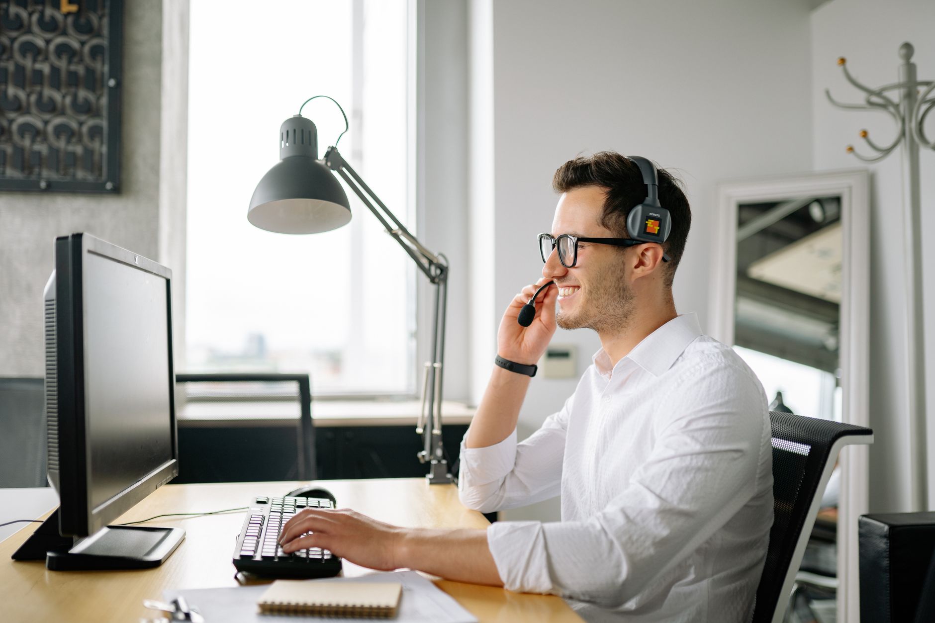 Smiling man wearing headset working at computer in bright office — illustrating: VoIP Providers for Central Florida Businesses: Which Offers the Best Local Support in 2026?